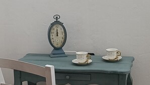 A small, teal-colored desk with a white chair, a vintage clock, and two teacups on the table.