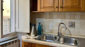 A kitchen with wooden cabinets, a stainless steel sink, and a window with a view of a building outside.