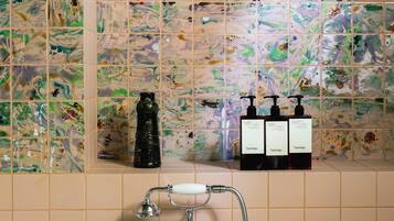 A bathroom with a shower, a sink, and a tiled wall with abstract designs. There are three bottles on the wall.