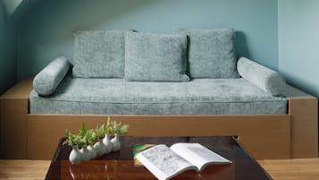 A modern loft bedroom with a sloped ceiling, a grey sofa, a glass coffee table, and two framed artworks.