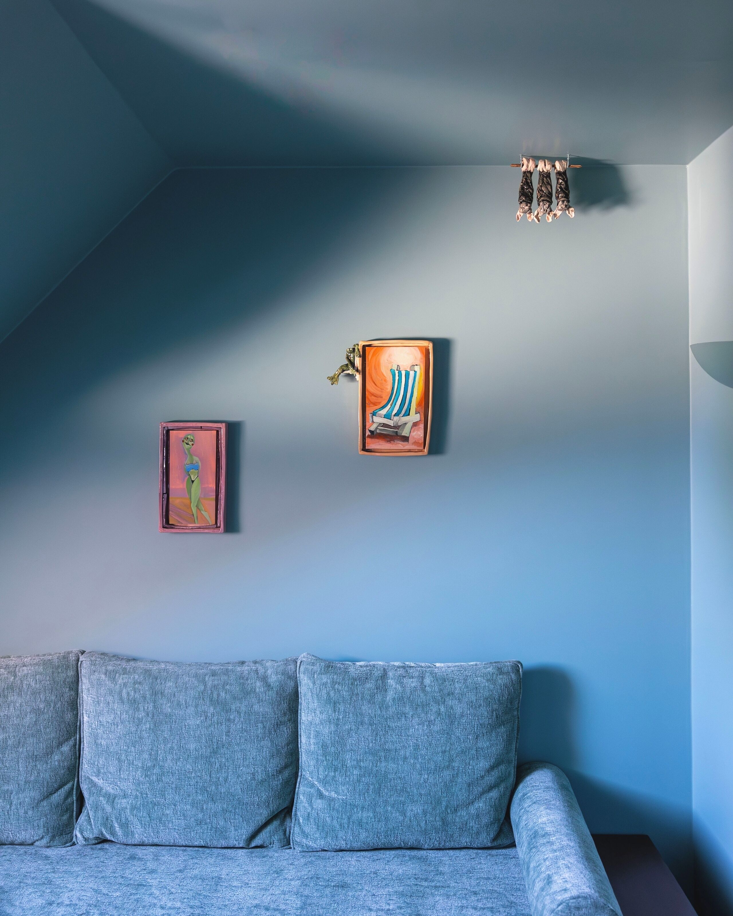 Una habitación con un sofá gris, un aplique de pared y dos cuadros enmarcados.