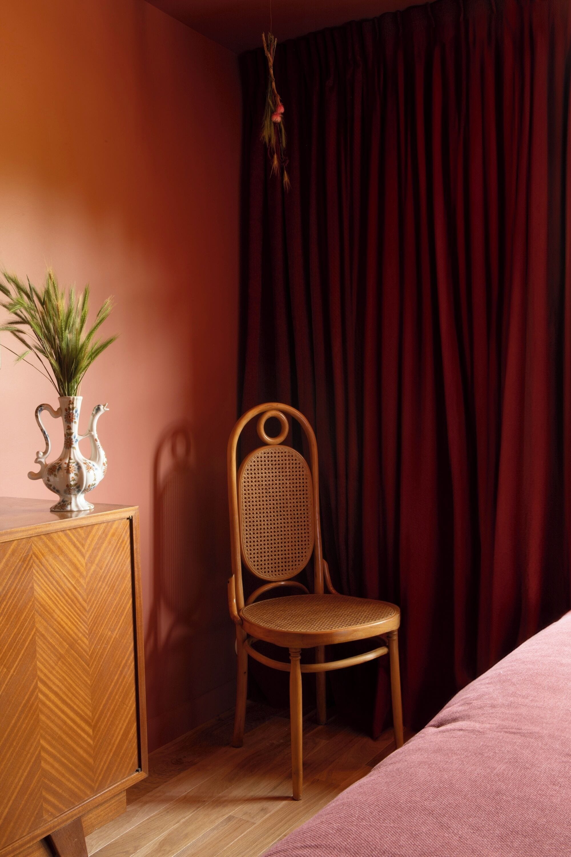 A room with a wooden cabinet, a wicker chair, and a bed.