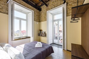 A bedroom with a bed, a wooden bench, a shelf with items, and a view of the outside.