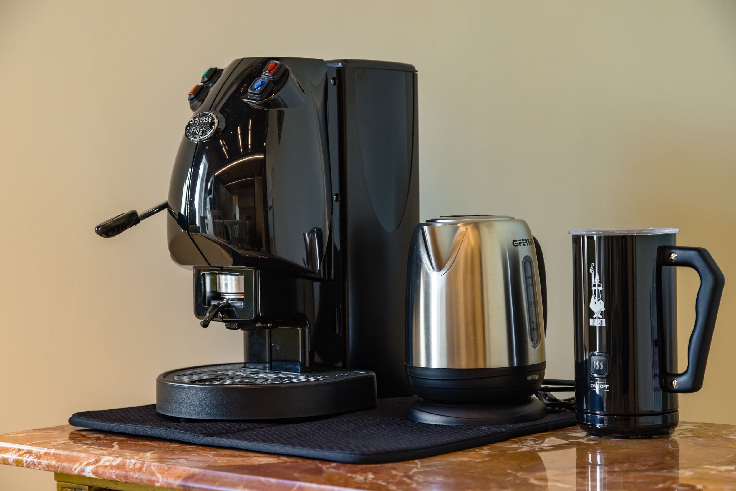 A coffee maker, a stainless steel electric kettle, and a black mug on a marble countertop.