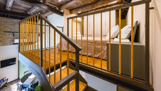 Une chambre de style loft moderne, avec un escalier en bois, un mur en pierre et un lit recouvert de linge de lit blanc.