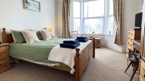 Une chambre à coucher avec un grand lit, une tête de lit en bois, une table de chevet, une commode, un téléviseur et une fenêtre avec des rideaux.