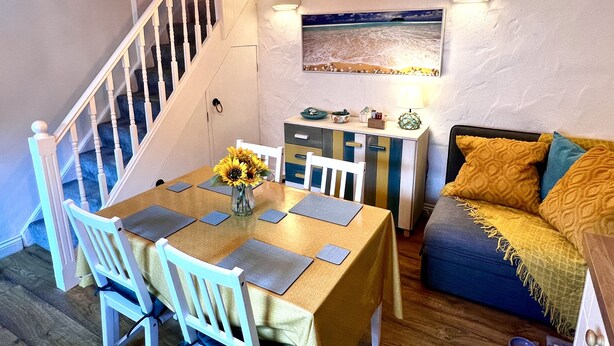 A dining area with a table set for four, a staircase, and a living area with a sofa and cushions.