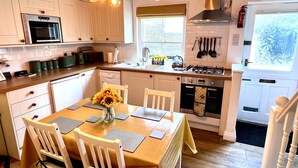 A kitchen with white cabinets, a dining table with chairs, a vase with sunflowers, and a hanging light fixture.