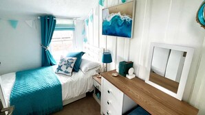 A bedroom with a bed, a bedside table, a lamp, a dresser, and a painting on the wall.