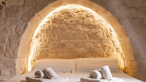 Una habitación con techo de arco de piedra, una cama con ropa de cama blanca y toallas enrolladas, y un colchón acolchado.