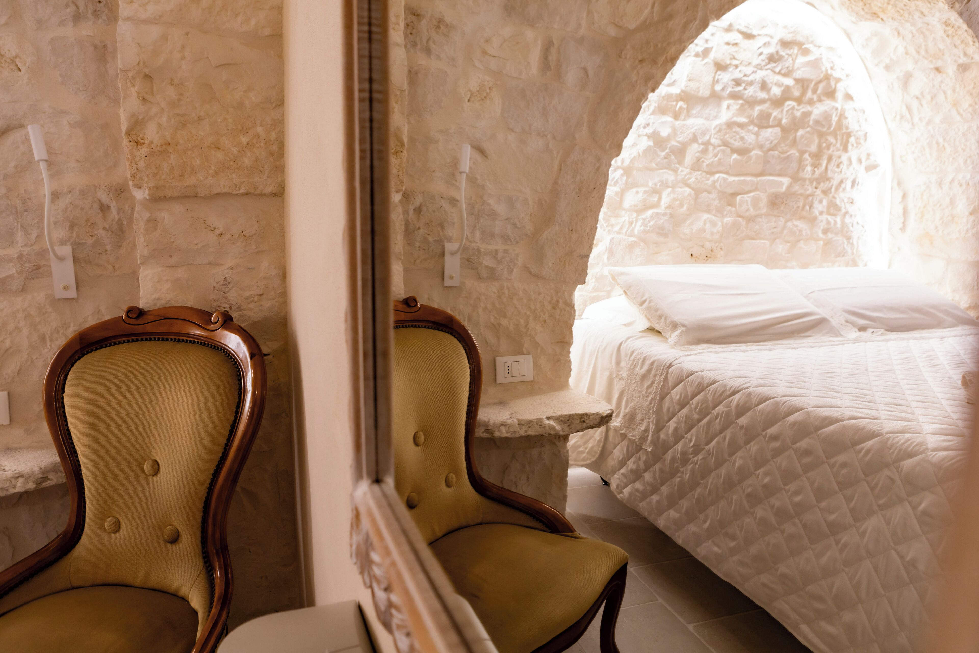 A room with a bed, a chair, and a stone wall.