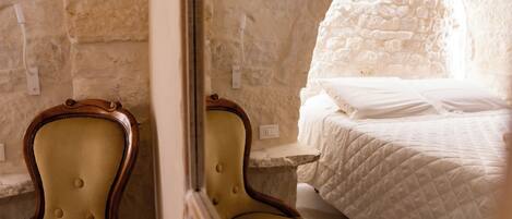 A room with a bed, a chair, and a stone wall.
