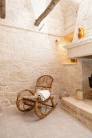 Una habitación rústica con paredes de piedra, una mecedora de mimbre, un estante blanco con adornos y una chimenea.
