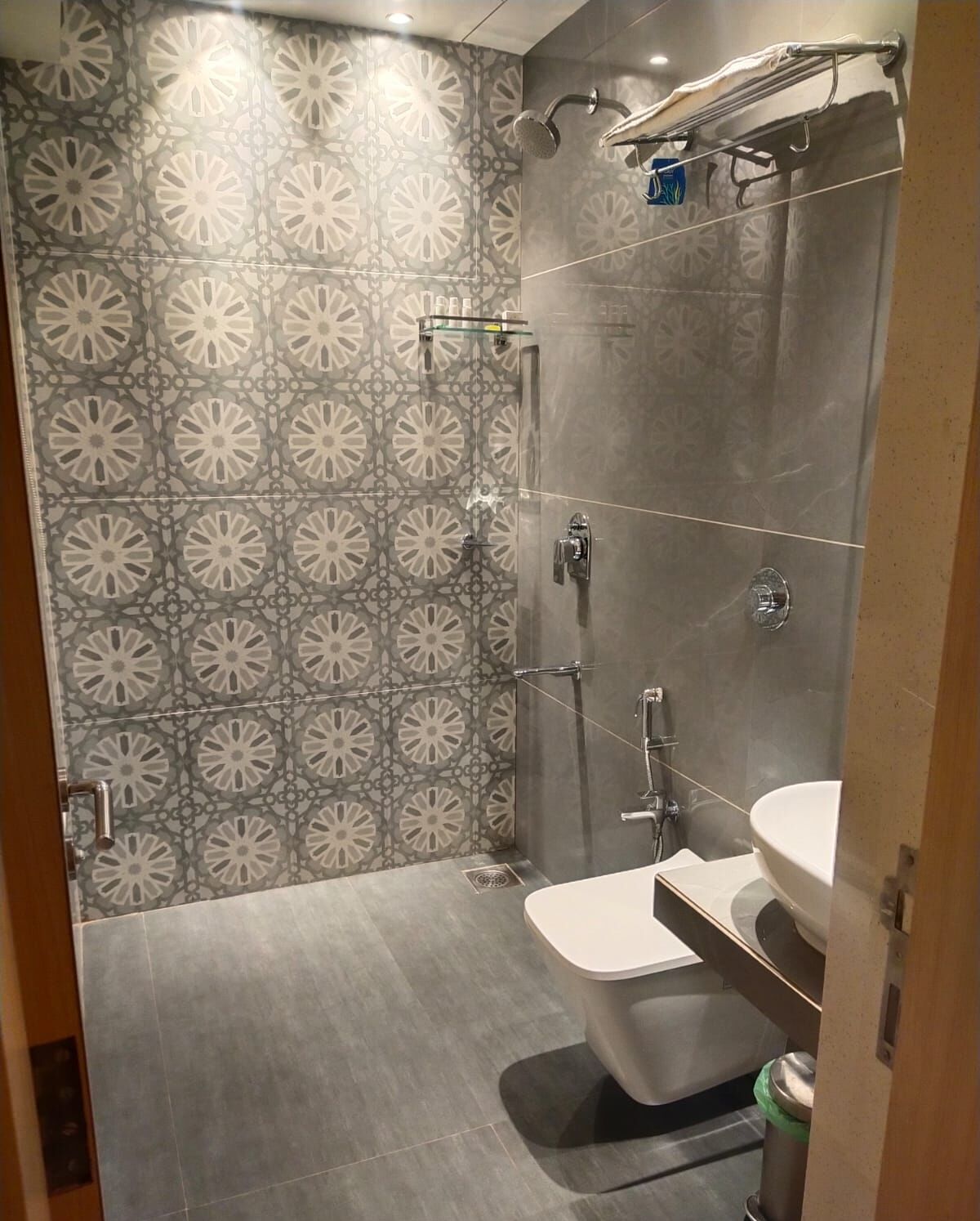 Uma casa de banho moderna com azulejos estampados, chuveiro, sanita e lavatório.