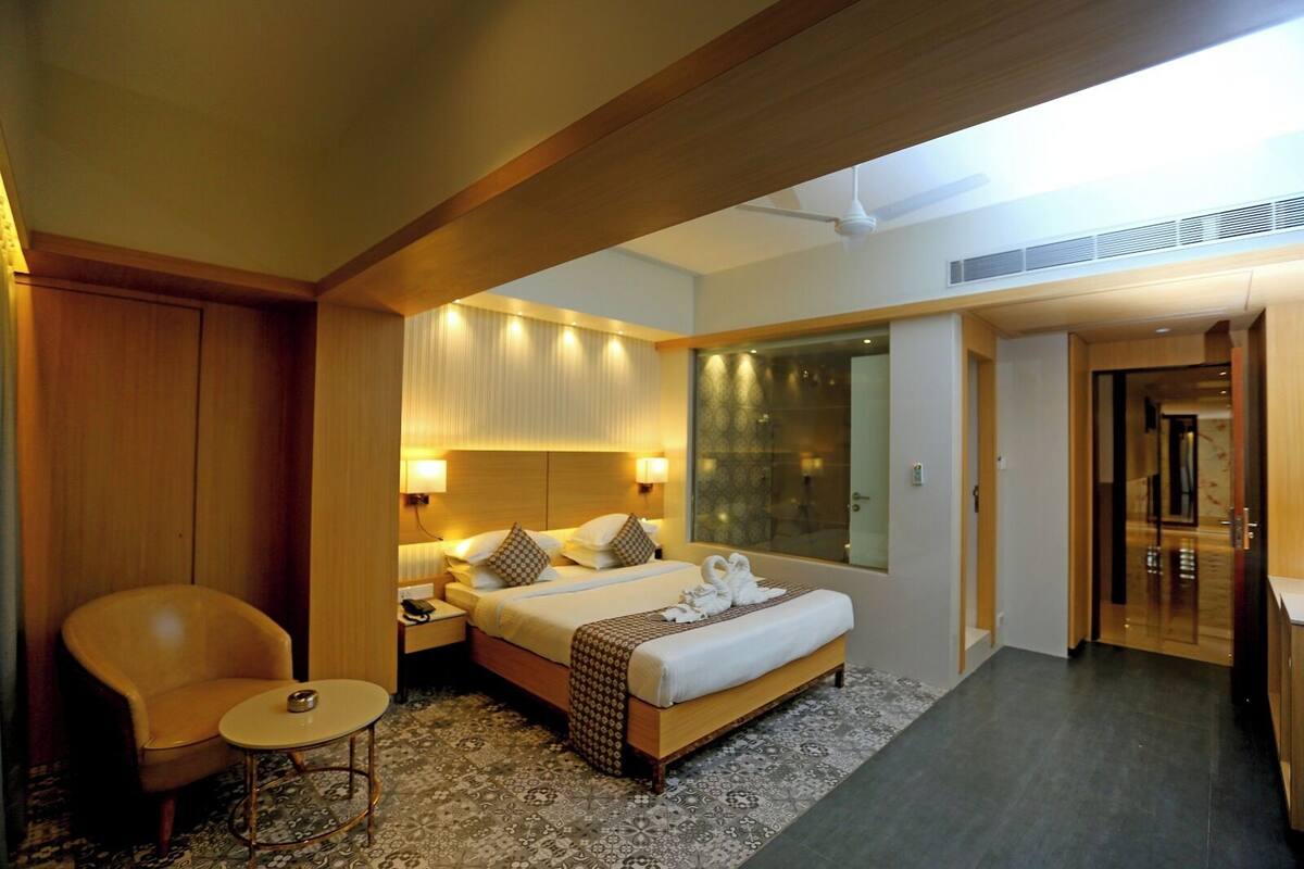 Una habitación de hotel moderna con una cama grande, una zona de estar con una silla y una mesita, y un área de ducha con mampara de vidrio.