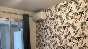 Une chambre d’hôtel avec deux lits, une grande fenêtre donnant sur un beau paysage, une armoire blanche et un papier peint à motifs floraux.