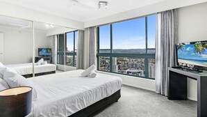 A modern hotel room with a large bed, a TV, and a city view through large windows.