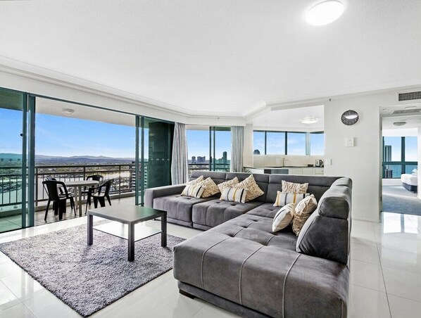 A modern living room with a grey sectional sofa, a small table, and a view of the city through large windows.