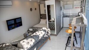 A modern living area with a grey tufted sofa, a flat-screen TV mounted on the wall, and a kitchen with a bar area. - TERRACE FLAT AT THE CENTER OF OLD CITY WITH JACUZZI (Istanbul)