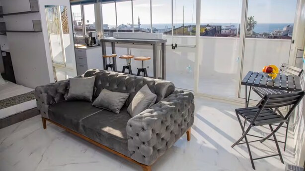 A modern living room with a grey tufted sofa, a small bar area, and a view of the cityscape. - TERRACE FLAT AT THE CENTER OF OLD CITY WITH JACUZZI (Istanbul)