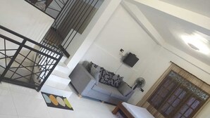 Une pièce comprenant un canapé, un lit, une fenêtre avec des rideaux, un ventilateur et un escalier avec une rampe.