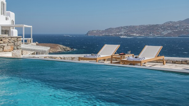 A poolside area with two lounge chairs and a stone structure, overlooking a clear blue sea and a distant coastline. - Esti Villa Melissa - Executive Luxury Villa (Mykonos)
