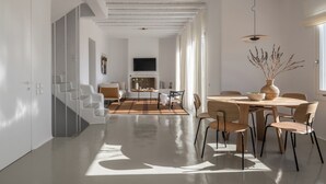 A spacious living area with a dining table, chairs, and a large window providing natural light. - Esti Villa Melissa - Executive Luxury Villa (Mykonos)