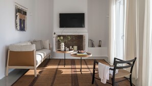 A modern living room with a sofa, a small table with a vase, a chair, a fireplace, and a TV mounted on the wall. - Esti Villa Melissa - Executive Luxury Villa (Mykonos)