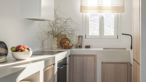 A modern kitchen with white cabinetry, a built-in oven, and a window above the sink. - Esti Villa Melissa - Executive Luxury Villa (Mykonos)