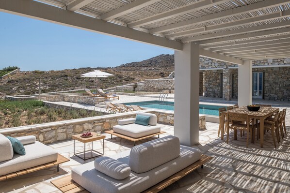 Un área de estar al aire libre techada, con piscina, paredes de piedra y vistas al paisaje.