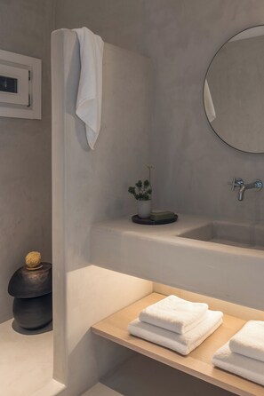 Un baño moderno con bañera, lavamanos y espejo. Hay un perchero con una toalla colgada, una pequeña planta en maceta y un jabonera.