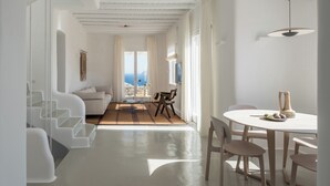 Un intérieur moderne et minimaliste, avec un escalier, un coin repas et une vue sur la mer.