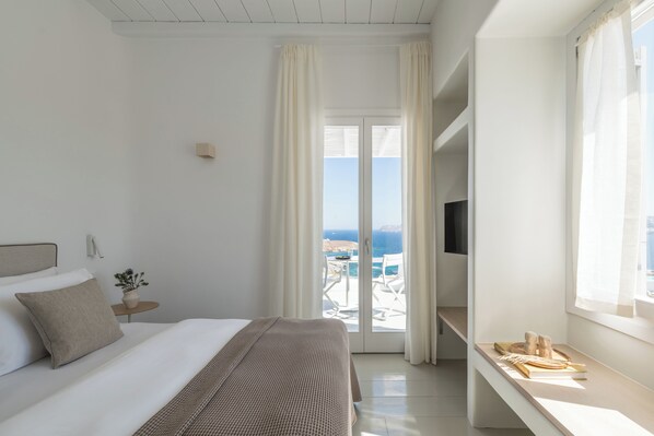 Habitación de hotel con cama, televisor, escritorio y vista al mar.
