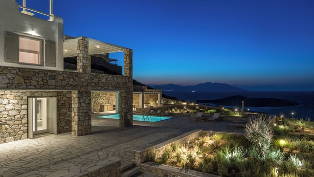 Une maison moderne à deux étages, avec une façade en pierre, une piscine et un espace salon extérieur.
