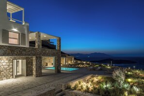 Una casa moderna de dos pisos con fachada de piedra, piscina y zona de estar exterior.