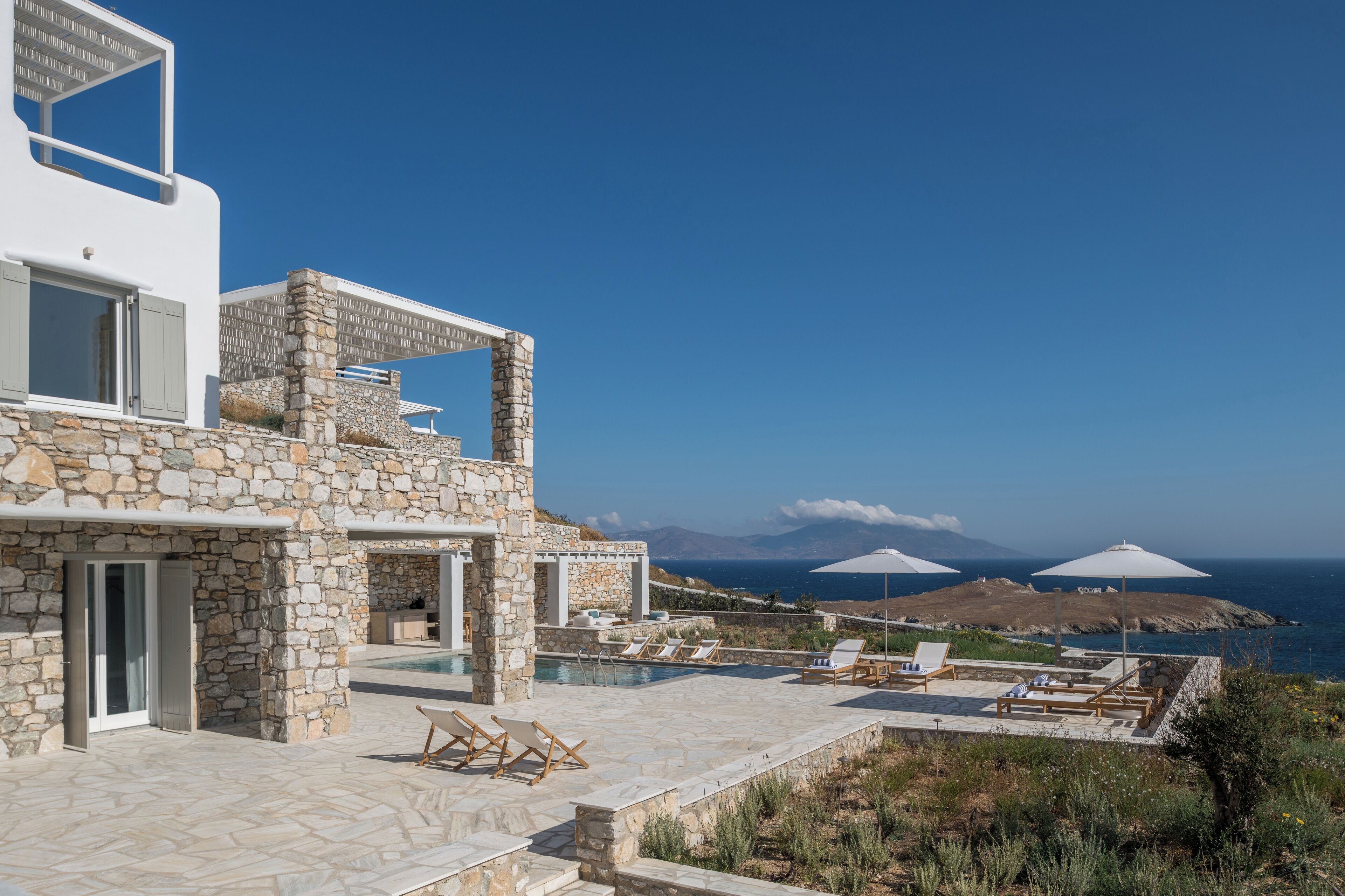 Un edificio moderno con pareti in pietra e un'area piscina con lettini e ombrelloni.