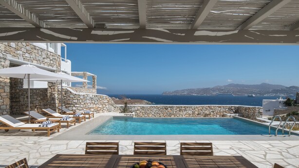 A poolside area with lounge chairs, a table, and a bowl of fruit.