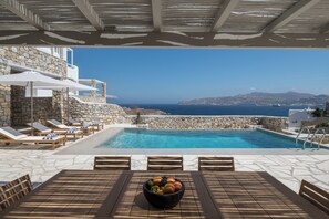 A poolside area with lounge chairs, a table, and a bowl of fruit. - Esti Villa Salvia - Executive Luxury Villa (Mykonos)