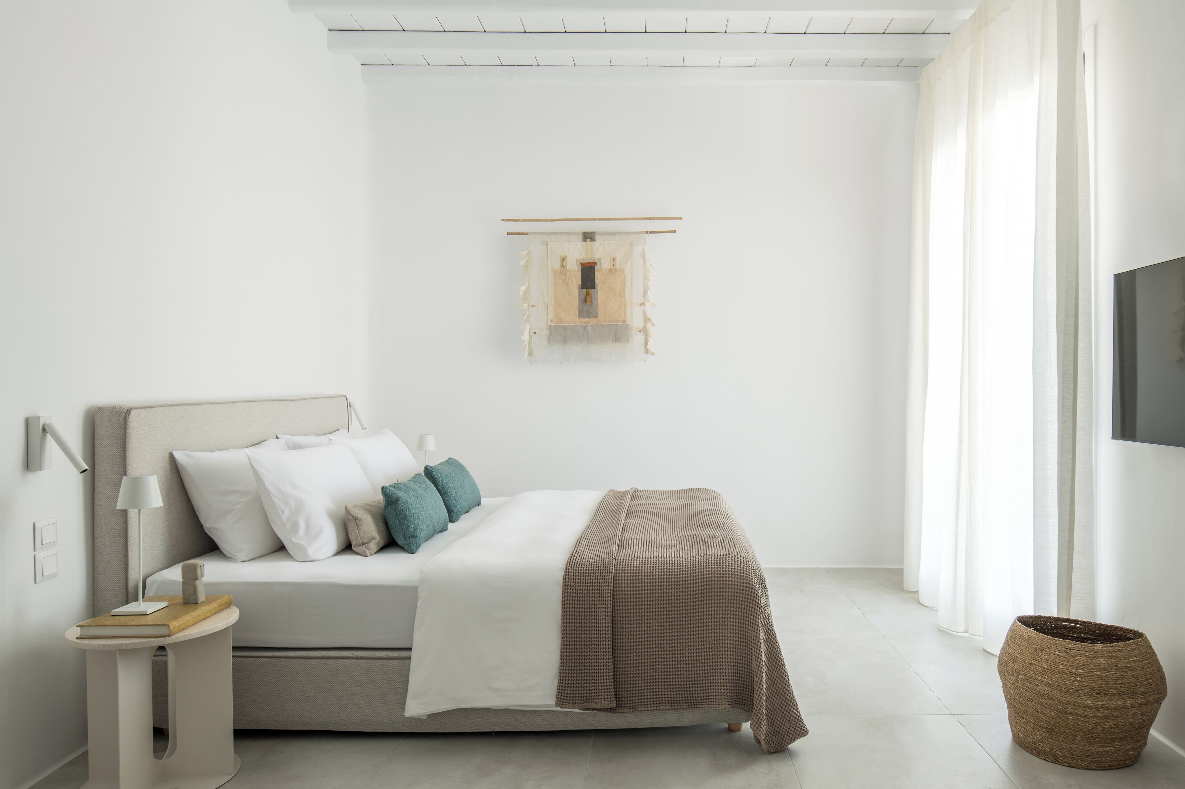 A minimalist bedroom with a bed, bedside table, lamp, and a mounted TV.
