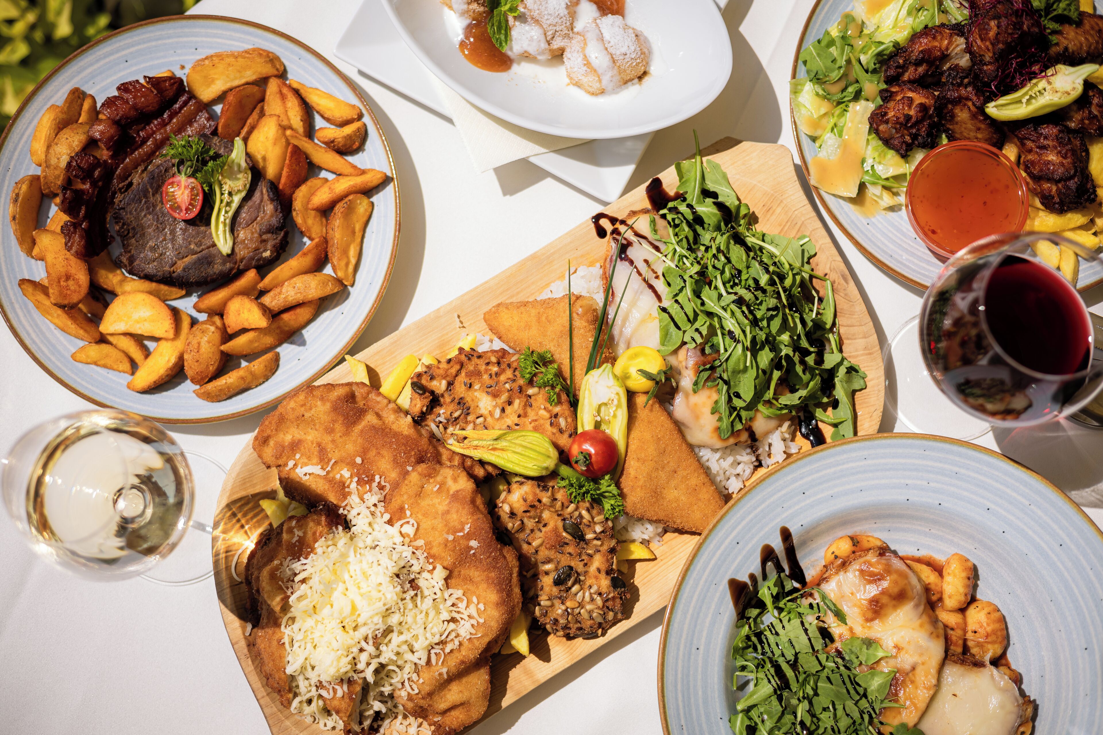 Variedad de platos, como carne, papas fritas y ensaladas, sugiriendo un ambiente de restaurante.