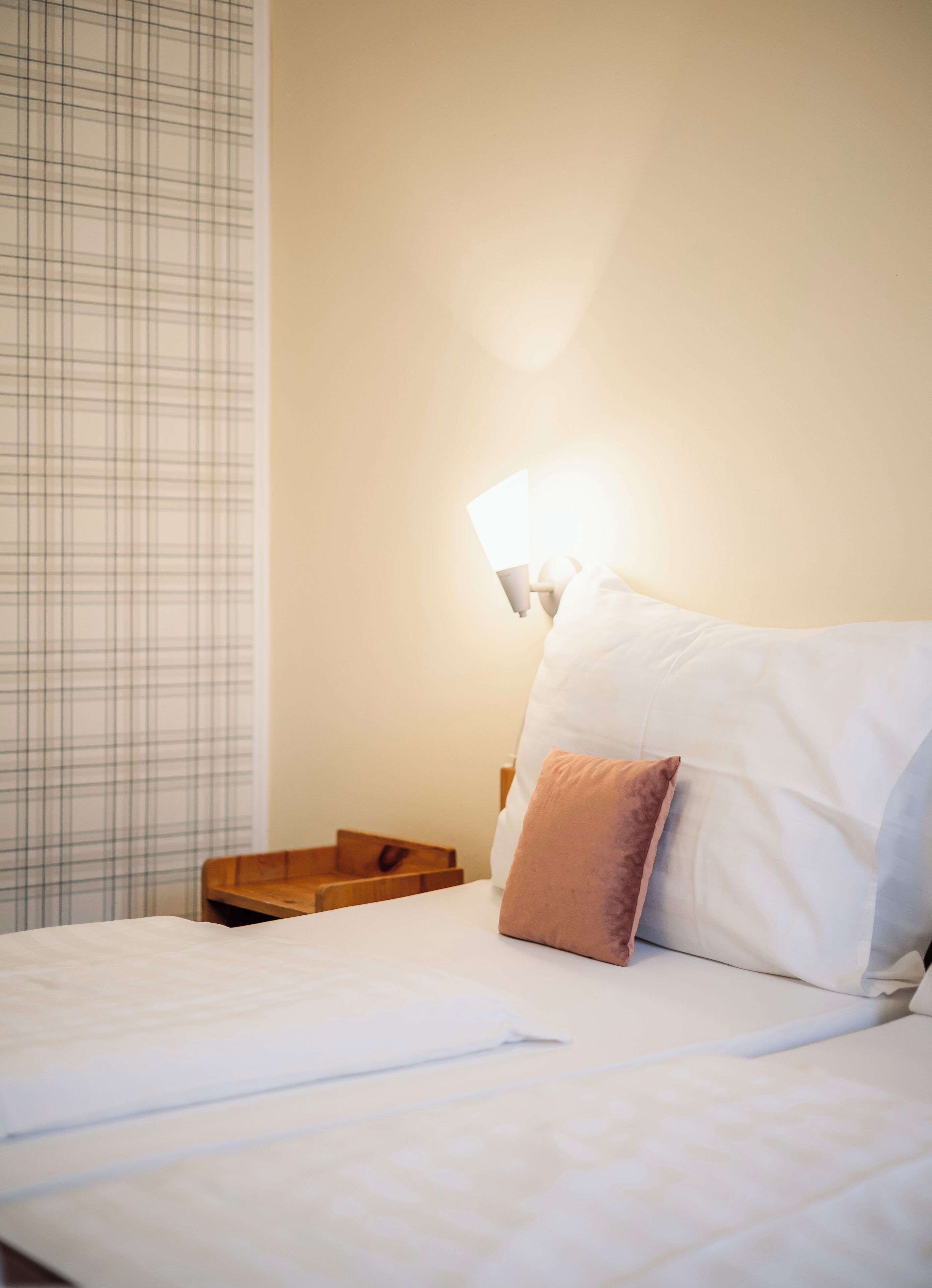 A neatly made bed with white and brown pillows, a wooden nightstand, and a wall-mounted lamp.