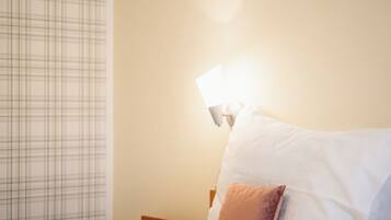 A neatly made bed with white and brown pillows, a wooden nightstand, and a wall-mounted lamp.