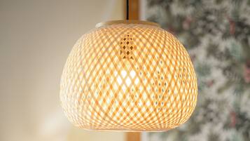 A hanging lamp with a woven pattern, a bed with a red pillow, and a floral wallpaper background.