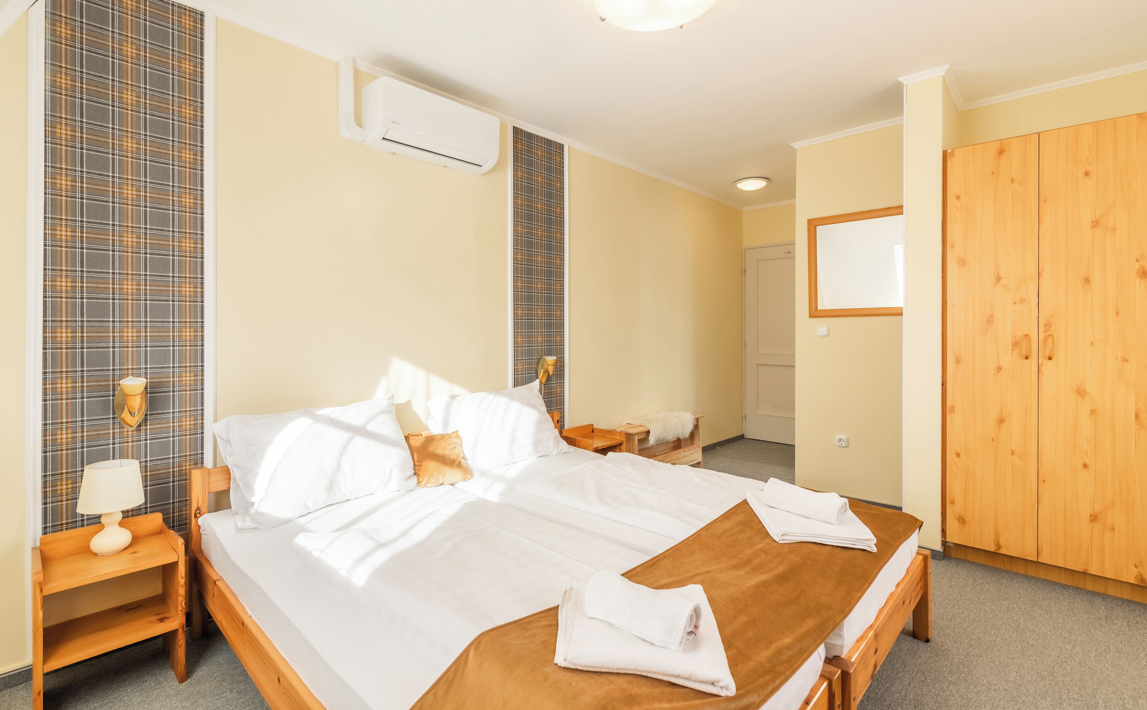 Habitación de hotel con una cama grande, un armario de madera, una mesita de noche con lámpara y un aire acondicionado instalado en la pared.