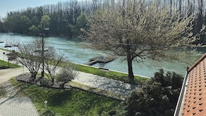 A riverside park with a paved walkway, benches, and trees. - Regia Panzió és Étterem (Halászi)