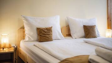 Una cama bien hecha con ropa de cama blanca y dos almohadas marrones, un cabecero de madera y una mesita de noche con una lámpara encendida.
