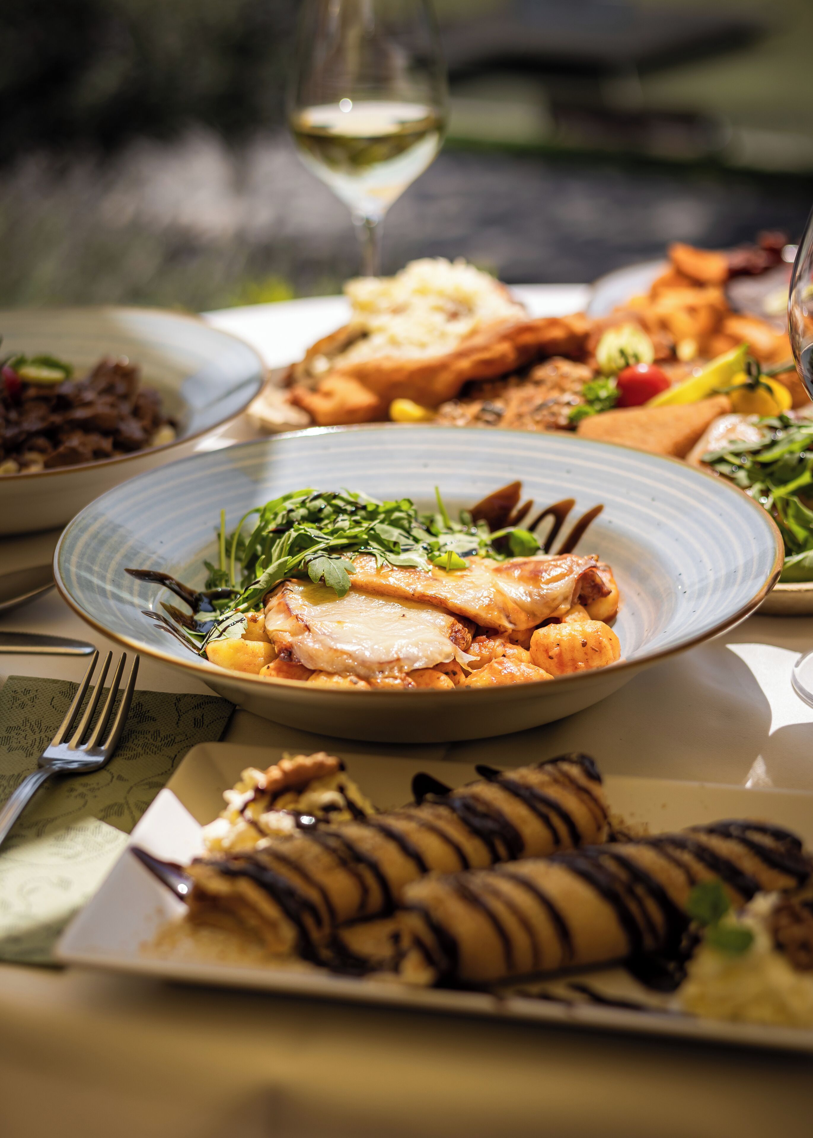 Una mesa con varios platos, incluyendo un plato con pollo, una copa de vino blanco y otros alimentos.