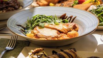 Una mesa con varios platos, incluyendo un plato con pollo, una copa de vino blanco y otros alimentos.