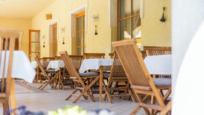 A row of wooden chairs with white tablecloths, arranged in a dining area with a tiled floor and beige walls. - Regia Panzió és Étterem (Halászi)