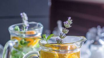 A pitcher of yellow beverage with a handle, garnished with a sprig of lavender, on a white surface.